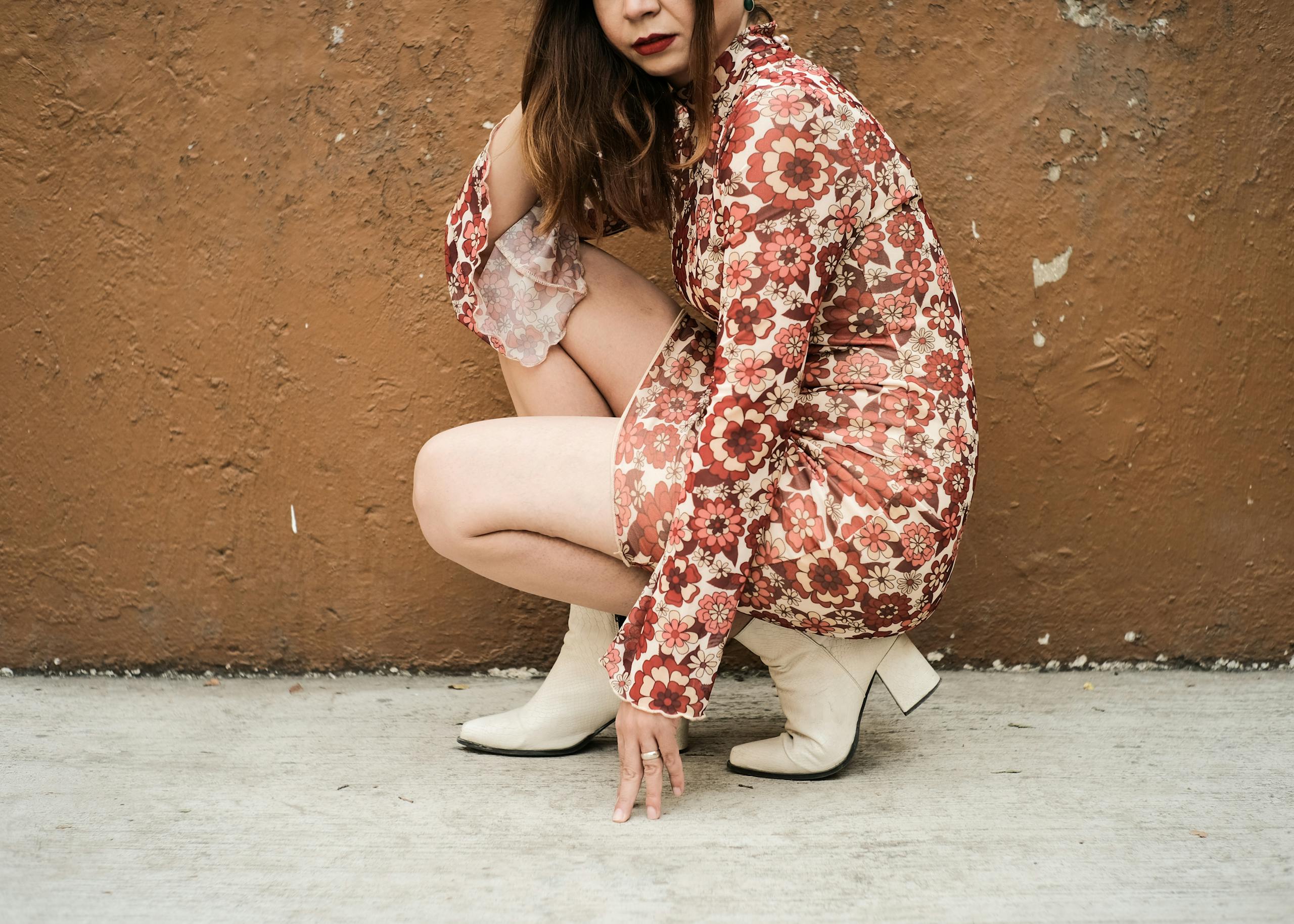 Young Brunette in a Dress and Boots Posing on the Background of a External Wall of a Building